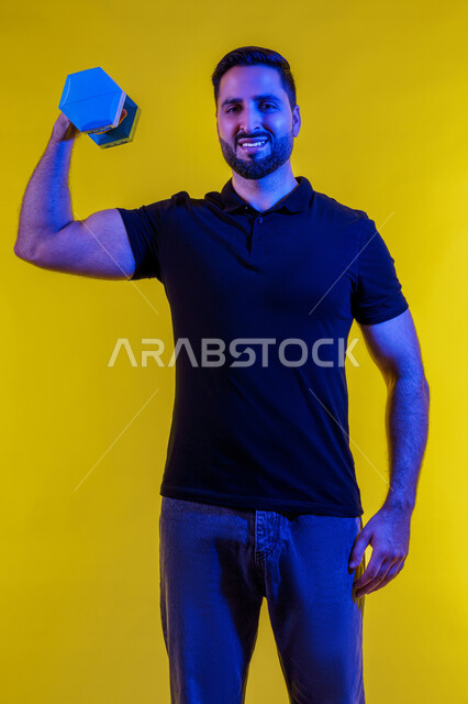 Gestures of strength and confidence, using iron weights, portrait of a young Arab Gulf Emirati man wearing casual clothes, bodybuilding, healthy lifestyle, interest in health and physical fitness, Saudi man practicing muscle strengthening activities, yellow background