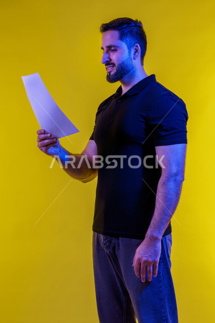 النظر الى كراسة الملاحظات، التفكير بالمستقبل، التأمل والتخطيط، رجل عربي خليجي سعودي يرتدي الزي االكاجوال يحمل بيده كراسه تدوين الملاحظات، افكار وحلول، التفكير بالمستقبل، بورتريه لشاب اماراتي تبدوعليه ايماءات التمعن والتركيز، خلفيه صفراء