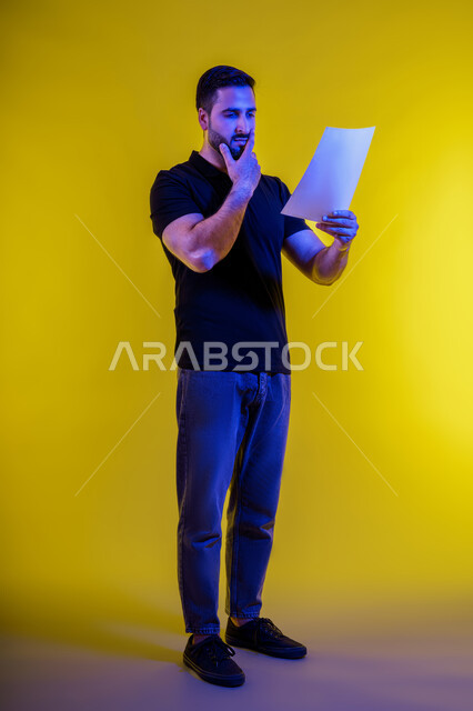 الحيرة والتفكير، التأمل والتخطيط، رجل عربي خليجي سعودي يرتدي الزي االكاجوال يحمل بيده كراسه تدوين الملاحظات، افكار وحلول، التفكير بالمستقبل، بورتريه لشاب اماراتي تبدوعليه ايماءات التمعن والتركيز، خلفيه صفراء