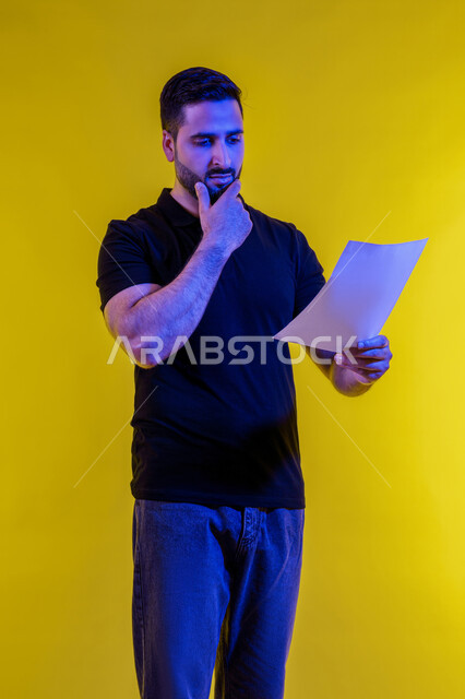 ايماءات وجه ويدين تدل على التفكير والحيرة، رجل عربي خليجي سعودي يرتدي الزي االكاجوال يحمل بيده كراسه تدوين الملاحظات، التأمل والتخطيط، افكار وحلول، التفكير بالمستقبل، بورتريه لشاب اماراتي تبدوعليه ايماءات التمعن والتركيز، خلفيه صفراء
