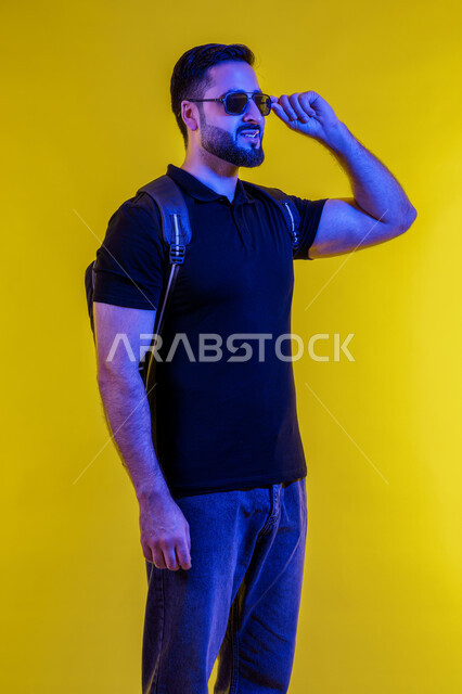 الاهتمام بالاناقة والمظهر الخارجي العصري للرجل، شاب اماراتي خليجي عربي يرتدي الزي الكاجوال ونظارات شمسية مبتسم، بورتريه لشاب عربي سعودي تظهر عليه ايماءات الثقة والابتسام، خلفية صفراء