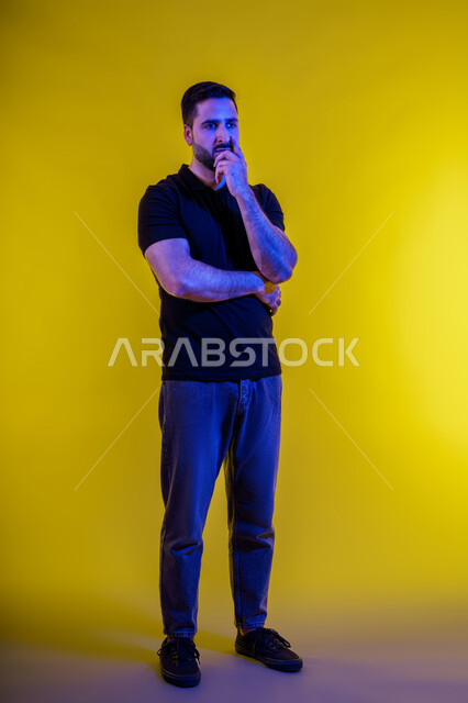 التركيز لإيجاد حل لمشكلةلشاب اماراتي، بورتريه لرجل عربي خليجي سعودي يرتدي الزي الكاجوال يضع يده على ذقنه بتعابير التفكير والتركيز بشيء ما، ايماءات شرود الذهن والحيرة والقلق، التأمل و التخطيط للمستقبل، الجسم بالطول الكامل , خلفية صفراء