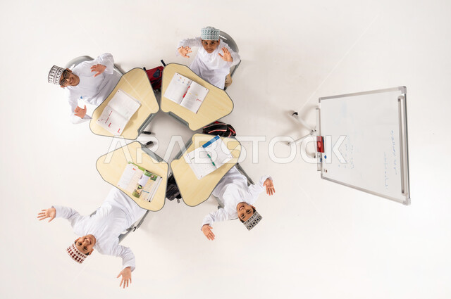 Group activities for teaching students in Omani schools, Gulf Arab Omani students wearing traditional dishdasha and kummah sitting on school desks, vertical overhead portrait of a Gulf Arab Omani teacher giving lessons on a whiteboard, interest in the educational process, white background