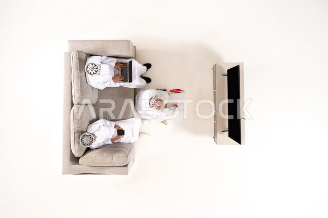 Watching TV shows, practicing fun hobbies, using modern technology during breaks, entertainment and fun during free time via laptop, vertical overhead portrait of an Omani Gulf Arab family wearing a dishdasha and kummah sitting in the living room, white background