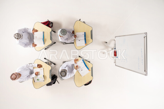The concept of interest in science and education in the Sultanate of Oman, Omani Gulf Arab students wearing dishdasha and kummah sitting in class, doing homework, vertical top portrait of a Saudi Gulf Arab teacher helping students with group activities, white background