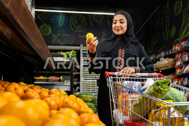 Benefit from offers and discounts, enjoy shopping in malls and commercial centers, an Arab Gulf Emirati woman buying lemons, a veiled Saudi woman wearing an abaya carrying a basket, buying products from the supermarket, agricultural products of her homeland, Saudi Arabia