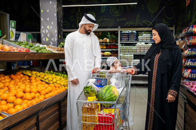 مشاركة الآراء وقضاء وقت ممتع في المراكز التجارية، عرض المنتجات والمواد الغذائيه على الارفف في السوبرماركت، ايماءات تدل على السعادة، زوجان عربيان خليجيان اماراتيان يرتديان الزي التقليدي يقومان بقضاء أوقات ممتعة بالتسوق واختيار اللوازم المنزليه برفقه ابنهم