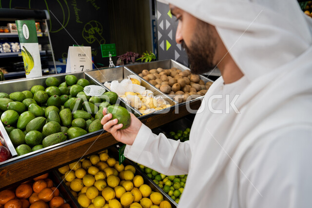 قضاء وقت ممتع في المركز التجاري, شراء الاحتياجات و المستلزمات المنزلية للمستهلك، صورة مقربه  لرجل عربى خليجي اماراتي يرتدي الكندورة و الغترة البيضاء يقوم بانتقاء الافوكادو، شراء الاحتياجات المنزلية من السوبرماركت، محاصيل زراعية اماراتيه
