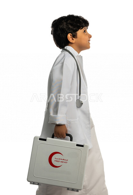 بورتريه بمنظر جانبي لفتى عربي خليجي سعودي ، يحمل بيده حقيبة الإسعافات الأولية ، يقوم بالسير بمفهوم لغة الجسد المختلفة ، يرتدي زي الطبيب ، الطبيب الصغير ، يحلم بأن يصبح طبيب ، المهنة المستقبلية ، مفهوم الطب والرعاية الصحية ، خلفية بيضاء