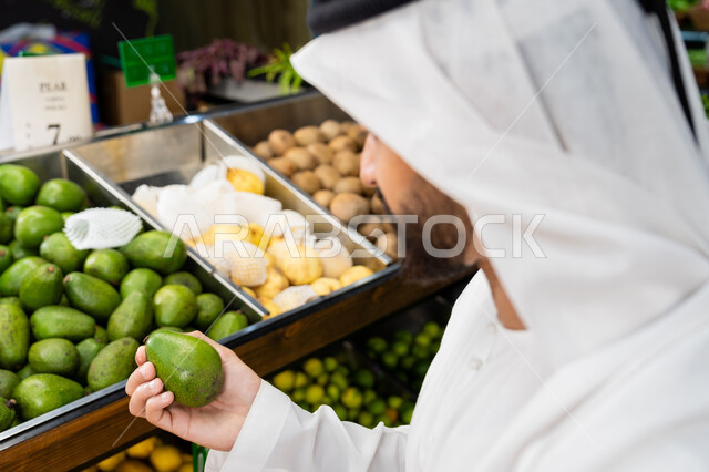الحفاظ على الرشاقة من خلال تناول المأكولات الصحية, متعه التسوق و اختيار الفاكهه الطازجه، صورة مقربه  لرجل عربى خليجي اماراتي يرتدي الكندورة و الغترة البيضاء يقوم بانتقاء الافوكادو، شراء الاحتياجات المنزلية من السوبرماركت، محاصيل زراعية اماراتيه
