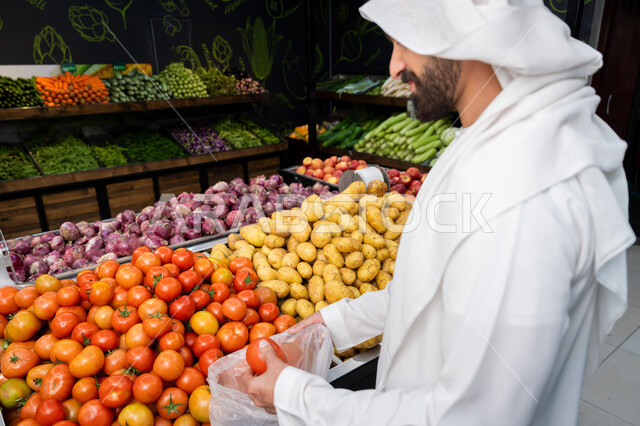 البحث عن أجود وأفضل أنواع الخضراوات والفواكه في المراكز التجارية، الخضراوات والفواكه الموسميه الطازجه ، رجل رجل عربي خليجي اماراتي يرتدي كندورة بيضاء يقوم بانتقاء الطماطم الحمراء، شراء المستلزمات المنزليه من السوبرماركت، محاصيل زراعية محلية اماراتية