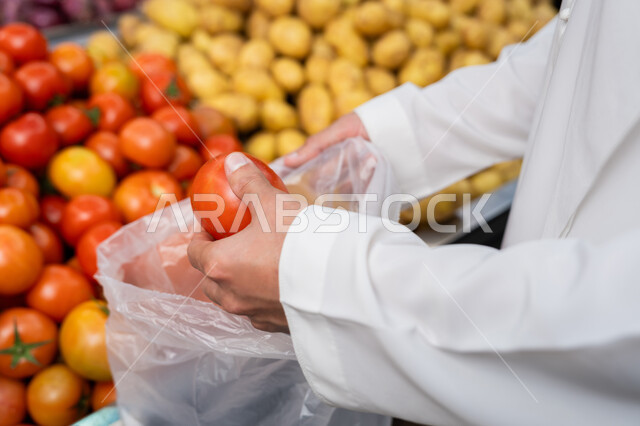 محاصيل زراعية اماراتية، الخضار الملون الطازج، شراء احتياجات المنزل من قسم الخضار والفواكه في المحلات، صورة مقربة ليد رجل عربي خليجي اماراتي يرتدي الكندورة يقوم بانتقاء الطماطم، قضاء وقت ممتع في التسوق في الأسواق واختيار الوجبات الخفيفة والأطعمة الصحية