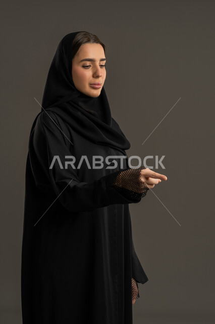 إيماءات وحركات يدين التوجيه لمكان معين ،الاشارة الى شئ ما ، بورتريه لامرأة عربية خليجية اماراتية ترتدي العباءة السوداء والحجاب ، سيدة سعودية تشير باصبع السبابة تجاه هدف ما ، خلفية سوداء.
