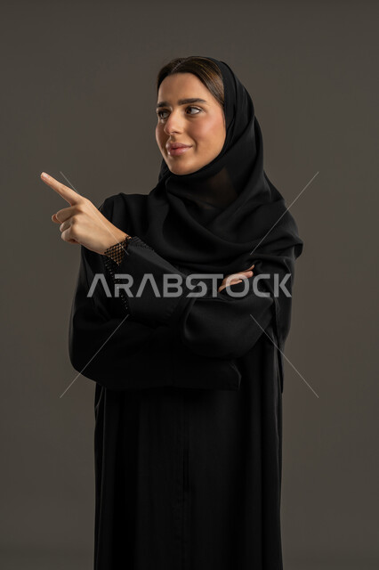 إيماءات وحركات يدين التوجيه لمكان معين ، بورتريه لامرأة عربية خليجية اماراتية ترتدي العباءة السوداء والحجاب ،  سيدة سعودية تشير باصبع السبابة تجاه هدف ما ، الاشارة لشئ ما ، خلفية سوداء.