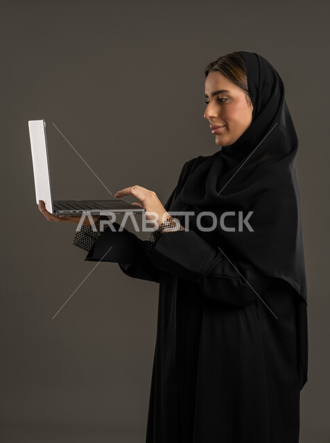 دمج التقنية والتكنولوجيا الحديثة في الحياة اليومية، ايماءات الاندماج والتركيز لإنجاز المهام  ،  ادارة العمل عن بعد ، إستخدام جهاز الحاسوب المحمول ، بورتريه لامراة عربية خليجية اماراتية تستخدم اللابتوب ، سيدة سعودية تقوم بتصفح الخدمات والتطبيقات عبر الانترنت ، مفهوم الإعلانات والتسويق الرقمي الإلكتروني ، خلفية سوداء .