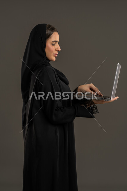 إنجاز مهام العمل عن بعد ، إستخدام جهاز الحاسوب المحمول ، بورتريه لامراة عربية خليجية اماراتية تستخدم اللابتوب ، إستخدام أجهزة تقنية حديثة ، سيدة سعودية تقوم بتصفح الخدمات والتطبيقات عبر الانترنت ،  مفهوم الإعلانات والتسويق الرقمي الإلكتروني ، خلفية سوداء .