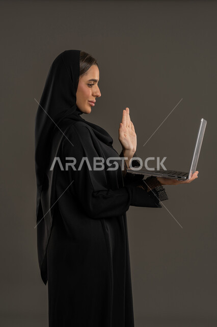اجراء مكالمات الفيديو عبر الانترنت  ، ايماءات الاندماج والتركيز لإنجاز المهام ، ادارة العمل عن بعد ، إستخدام جهاز الحاسوب المحمول ، بورتريه لامراة عربية خليجية اماراتية تمسك نظاره بيدها و جهاز اللابتوب ، إستخدام أجهزة تقنية حديثة ، سيدة سعودية تقوم بتصفح الخدمات والتطبيقات الحديثة ، مفهوم الإعلانات والتسويق الرقمي الإلكتروني ، خلفية سوداء .