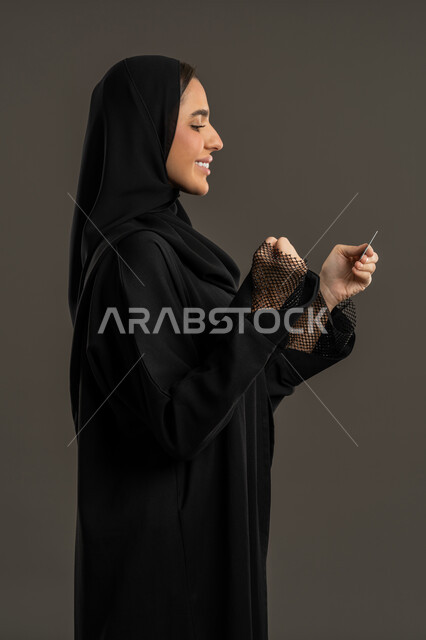 سهولة الشراء والدفع عن طريق بطاقة الإئتمان البنكية، إمكانية تسديد الفواتير بالتقنيات الحديثة، بورتريه من الجانب لإمرأة عربية خليجية اماراتية مبتسمة ترتدي العباءة السوداء والحجاب تمسك بيدها بطاقة الصراف، سيدة سعودية تنظر الى البطاقة الالكترونية بإيماءات وتعابير السعادة والفرح ، خلفية سوداء.
