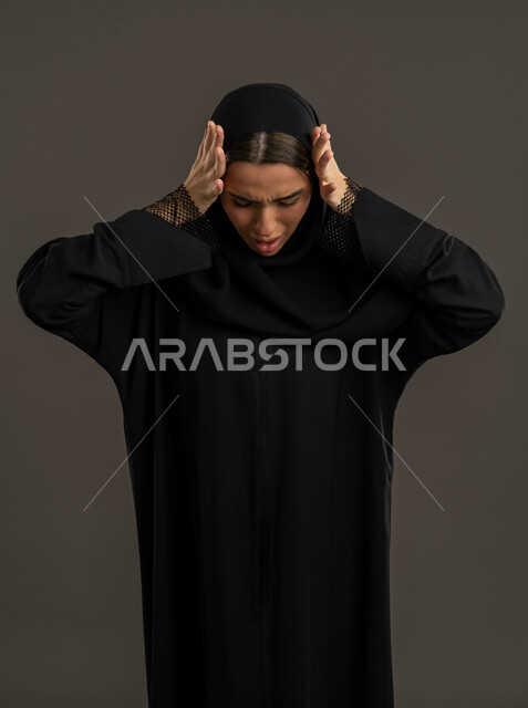 الشعور بالمفاجأة والصدمة، الانزعاج والاستغراب من شيء ما، بورتريه لإمرأة عربية خليجية اماراتية ترتدي العباءة السوداء والحجاب تضع يديها على رأسها تعجبا بحدوث أمر ما، سيدة سعودية تنظر إلى الاسفل بإيماءات الدهشة والذهول، خلفية سوداء .