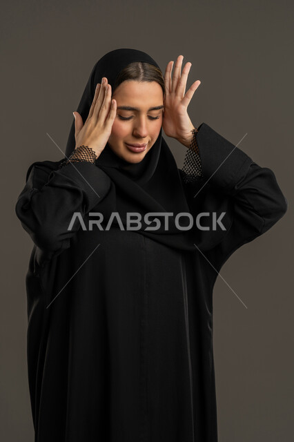 الانزعاج والدهشة والذهول من شئ ما ، الشعور بالمفاجأة والصدمة، بورتريه لإمرأة عربية خليجية اماراتية ترتدي العباءة السوداء والحجاب تضع يديها على رأسها تعجبا بحدوث أمر ما، سيدة سعودية تنظر إلى الاسفل بإيماءات الاستغراب ، خلفية سوداء .