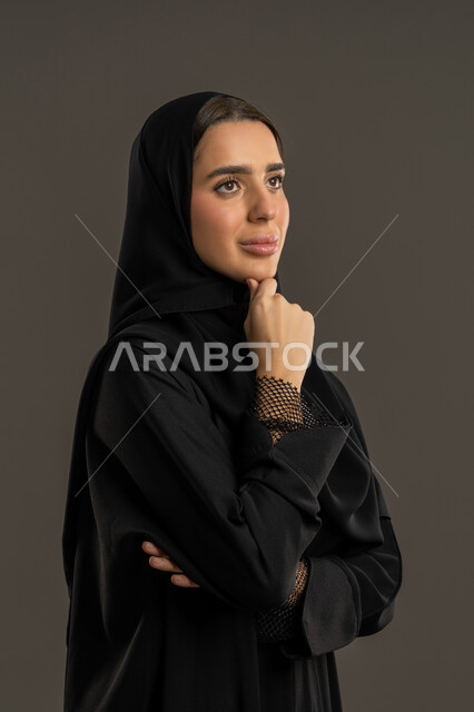 شرود الذهن في موضوع معين ، بورتريه مقرب لسيدة عربية خليجية اماراتية ترتدي العباءة السوداء والحجاب ، تنظر الى شئ ما بتعابير الاندماج و الحيرة ، سيدة سعودية  تضع يدها على ذقنها بايماءات التفكير ، محاولة إيجاد حل لمشكلة ما ، خلفية سوداء .