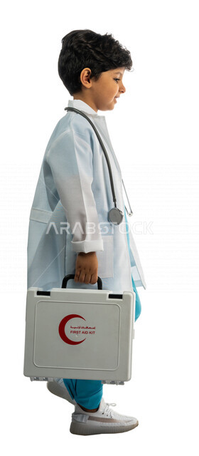بورتريه بمنظر جانبي لفتى عربي خليجي سعودي ، يحمل بيده حقيبة الإسعافات الأولية ، يقوم بالسير بمفهوم لغة الجسد المختلفة ، يرتدي زي الطبيب ، الطبيب الصغير ، يحلم بأن يصبح طبيب ، المهنة المستقبلية ، مفهوم الطب والرعاية الصحية ، خلفية بيضاء