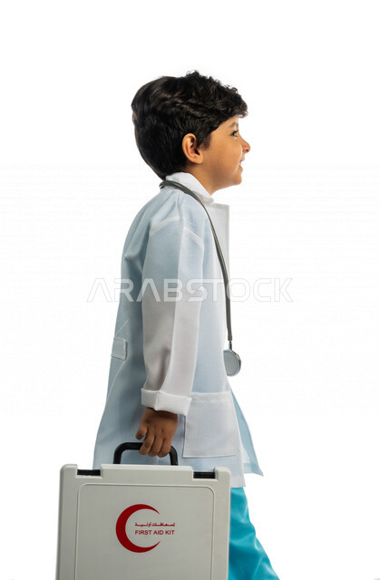 بورتريه بمنظر جانبي لفتى عربي خليجي سعودي ، يحمل بيده حقيبة الإسعافات الأولية ، يقوم بالسير بمفهوم لغة الجسد المختلفة ، يرتدي زي الطبيب ، الطبيب الصغير ، يحلم بأن يصبح طبيب ، المهنة المستقبلية ، مفهوم الطب والرعاية الصحية ، خلفية بيضاء