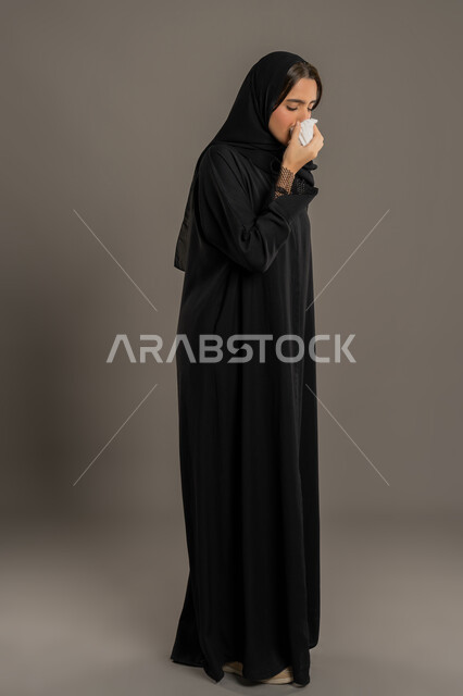 الإصابة بفايروس كورونا كوفيد19، الشعور بالتعب والمرض، استعمال المناديل الورقية أثناء العطس، بورتريه لامرأه عربيه خليجيه اماراتية محجبة ترتدي عباءة سوداء، إيماءات وجه ويدين تدل على العطاس، شابة سعودية مريضة، صورة لكامل الجسم، خلفية سوداء