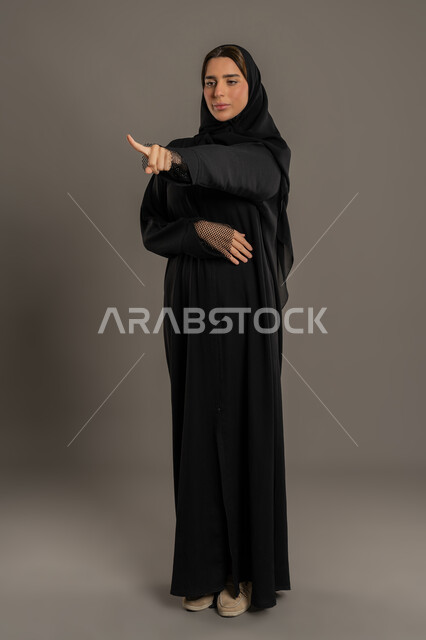 إلقاء اللوم و الاتهام، طلب التوقف عن فعل الأخطاء، امرأة خليجية اماراتية تشعر بالإنزعاج والرغبة بالإنتقام، بورتريه  لسيدة عربية سعودية ترتدي العباءة السوداء ترفع اصبع السبابه لتحديد شخص ما ( أنت )، الجسم بالطول الكامل, خلفية سوداء
