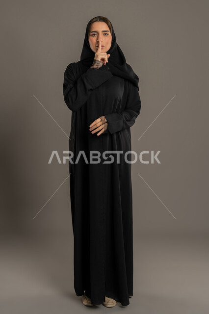 التوقف عن الكلام, تعابير وجه تدل على الغضب , بورتريه لأمرأه عربية خليجية اماراتية محجبة ترتدي العباءه السوداء ,إيماءات يدين تدل على طلب الهدوء و عدم الإزعاج, سيدة سعودية تأمر بالصمت والسكوت , الجسم بالطول الكامل، خلفية سوداء