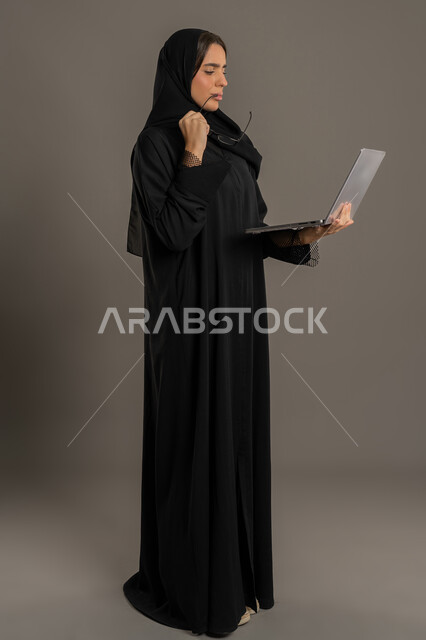 إدارة شؤون الأعمال وتنظيمها، صورة لسيدة عربية خليجية اماراتية تقوم بالعمل على الحاسب المحمول، التفكير والتخطيط ، سيده سعودية تستخدم الحاسب المحمول لإنجاز المهام،خلفية لكامل الجسم, خلفية سوداء