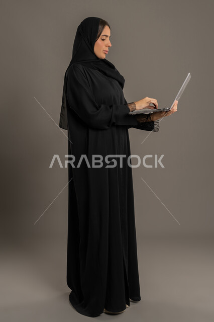 تصفح الإنترنت وإستخدام اجهزة تقنية حديثة، إدارة شؤون الأعمال وتنظيمها، صورة لسيدة عربية خليجية اماراتية تقوم بالعمل على الحاسب المحمول، العمل لتحقيق الاهداف والاستراتيجيات،  سيده سعودية تستخدم الحاسب المحمول لإنجاز المهام،خلفية لكامل الجسم, خلفية سوداء