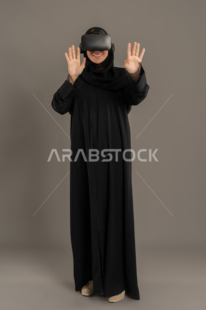 التفاعل مع الواقع الافتراضي، الشعور بالمتعة والتسلية بمحاكاة العالم الخيالي, الأجهزة التكنولوجية والتقنيات الحديثة، بورتريه لامرأة عربية خليجية اماراتية محجبة ترتدي نظارات في آر ثلاثية الأبعاد، سيده سعوديه تقوم بمحاولة لمس العناصر الخيالية،الجسم بالطول الكامل، خلفية سوداء