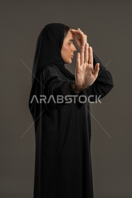 عدم تخطي الحدود في الكلام, بورتريه من الجانب لسيدة عربية خليجية امارتيه محجبه ترتدي العباءه السوداء  تغطي وجهها بيدها و تشير بكفة يدها الأخرى بإيماءات و تعابير وجه و يدين تدل على التوقف و الابعاد،شابة سعودية تشعر بالإنزعاج و الرفض والإمتناع, خلفية سوداء