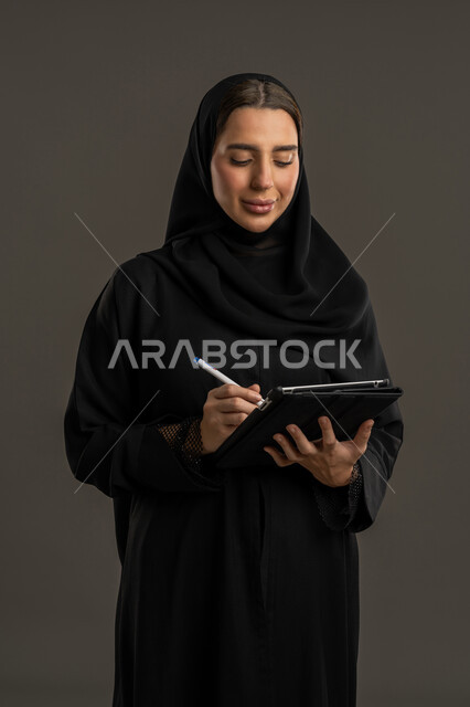 A collection of work papers, following up on correspondence and records, a portrait of a veiled Emirati Gulf Arab woman wearing a black abaya, holding a paper holder in her hands, taking notes, a Saudi woman completing the required tasks, black background