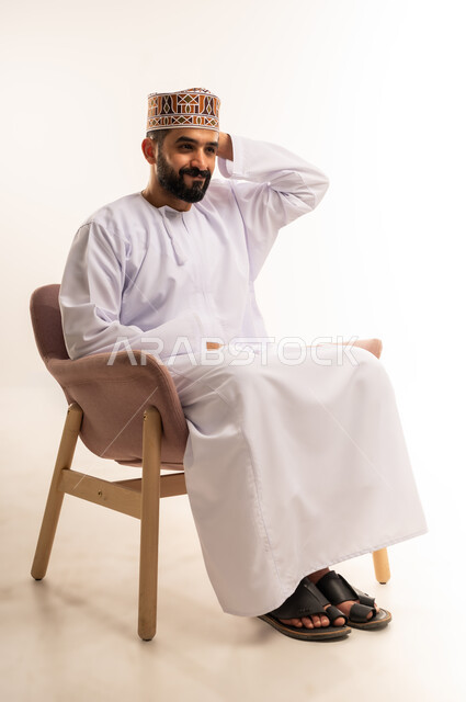 الشعور بالدهشة والصدمة والذهول, مشاهدة ومتابعة مباراة كرة القدم، بورتريه لرجل عربي خليجي عماني يرتدي الدشداشة والكمة يجلس على كرسى مريح يضع يديه خلف رأسه بايماءات الهزيمة ، المباريات والألعاب الرياضية، خلفية بيضاء .