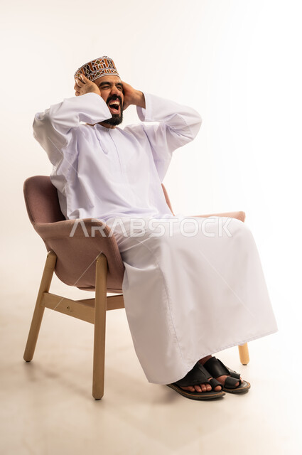 قضاء وقت ممتع بمتابعة المباراة، بورتريه لرجل عربي خليجي عماني يرتدي الدشداشة والكمة يجلس على كرسى مريح يضع يديه خلف رأسه بايماءات الصدمة والاندهاش، المباريات والألعاب الرياضية، خلفية بيضاء .