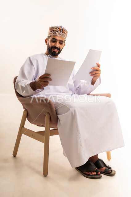 Using white paper to record important notes and information, tools for writing down daily tasks, a portrait of an Arab Gulf Omani man wearing a dishdasha and a kummah holding papers in his hand, with gestures of concentration and contemplation, a full-length body image, a white background.