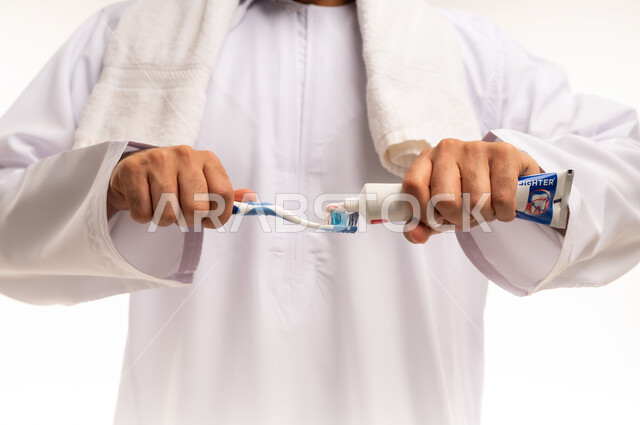 ادوات النظافة الشخصية ، استخدام منتجات محلية وطنية، المحافظة على ابتسامة بيضاء، تجنب التسوس وأمراض اللثة، مفهوم العناية والإهتمام بصحة الأسنان، روتين نظافة الفم اليومية، بورتريه مقرب ليد رجل عربي خليجي عماني يقوم بتنظيف أسنانه باستخدام الفرشاة والمعجون، خلفية بيضاء .