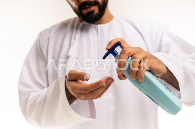 ترطيب وتفتيح البشرة، خطوات تنظيف البشرة، استخدام الكريمات ومكونات التجميل الشبابية، مفهوم العناية والاهتمام بنضارة البشرة وتحسينها، صورة مقربة ليد رجل عربي خليجي عماني يرتدي الدشداشة والكمة يحمل بيده عبوة لكريم مرطب، خلفية بيضاء.