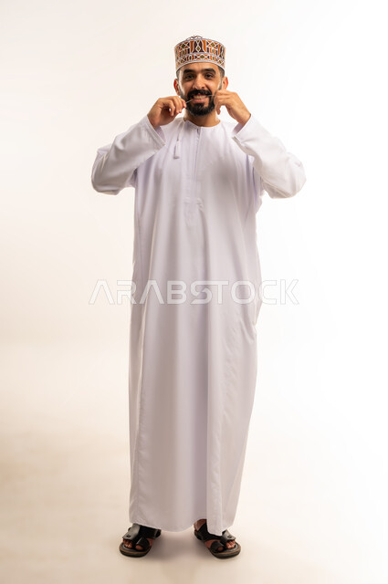 التأكد من نظافة الأسنان بعد تناول الطعام ، تنظيف الأسنان بالخيط السني ، الاهتمام بالأناقة والمظهر الخارجي، المحافظة على ابتسامة بيضاء، مفهوم العناية بصحة الفم، بورتريه لرجل عربي خليجي عماني يرتدى الدشداشة والكمة ، الجسم بالطول الكامل ، خلفية بيضاء .