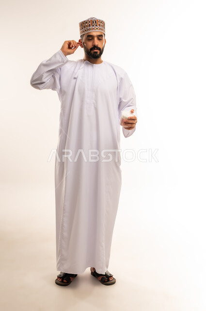 تنظيف الأسنان بالخيط السني ، الاهتمام بالأناقة والمظهر الخارجي، المحافظة على ابتسامة بيضاء، مفهوم العناية بصحة الفم، التأكد من نظافة الأسنان بعد تناول الطعام، بورتريه لرجل عربي خليجي عماني يرتدى الدشداشة والكمة ، الجسم بالطول الكامل ، خلفية بيضاء .