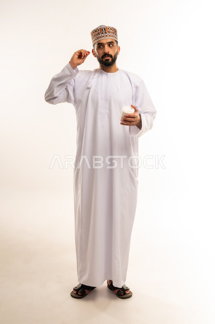 استخدام الخيط السني ، الاهتمام بالأناقة والمظهر الخارجي، المحافظة على ابتسامة بيضاء، مفهوم العناية بصحة الفم، التأكد من نظافة الأسنان بعد تناول الطعام، بورتريه  لرجل عربي خليجي عماني يرتدى الدشداشة والكمة ، يقوم بتنظيف أسنانه ، صورة الجسم بالكامل، خلفية بيضاء .
