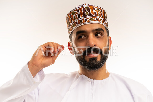 روتين نظافة الفم ، استخدام الخيط السني ، الاهتمام بالأناقة والمظهر الخارجي، المحافظة على ابتسامة بيضاء، مفهوم العناية بصحة الفم، التأكد من نظافة الأسنان بعد تناول الطعام، بورتريه مقرب لرجل عربي خليجي عماني يرتدى الدشداشة والكمة ، يقوم بتنظيف أسنانه ، خلفية بيضاء .