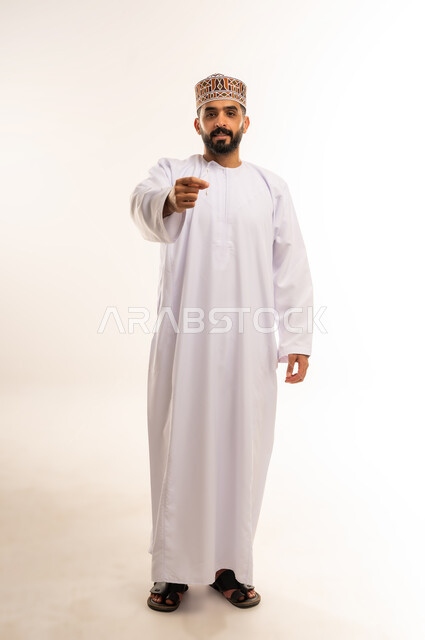 المحافظة على ابتسامة بيضاء، مفهوم العناية بصحة الفم، التأكد من نظافة الأسنان بعد تناول الطعام، الاهتمام بالأناقة والمظهر الخارجي، بورتريه  لرجل عربي خليجي عماني يرتدى الدشداشة والكمة ، يقوم بتنظيف أسنانه باستخدام الخيط السني، صورة الجسم بالكامل، خلفية بيضاء .