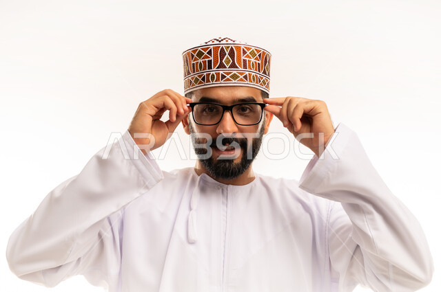 استخدام البصريات لتوضيح الرؤية، بورتريه مقرب لرجل عربي خليجي عماني يرتدي الدشداشة والكمة ,يلبس النظارات الطبية وينظر الى الكاميرا بإيماءات السعادة ، العدسات الخاصة بضعف النظر ، مفهوم الضبابية وعدم وضوح الرؤية ، خلفية بيضاء .