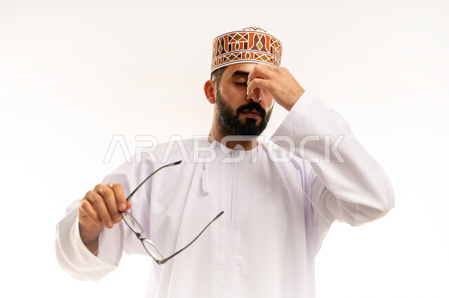 الشعور بالإرهاق وفقدان التركيز , الاحساس بالشقيقة والصداع النصفي ، النسيان ومحاولة تذكر شيء ما، بورتريه مقرب لرجل عربي خليجي عماني يرتدي الدشداشة والكمة ،يضع يده على عينه ويغمضها ، الرؤية من خلال العدسات الطبية, استخدام البصريات لتوضيح الرؤية، خلفية بيضاء .