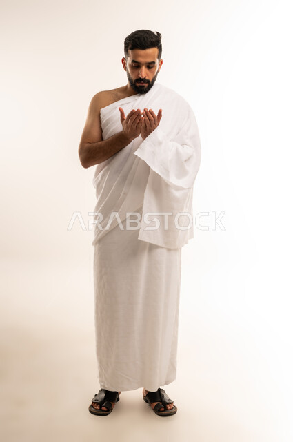 الخشوع والخضوع لله تعالى عند الدعاء، العبادة والطاعة والتقرب الى الله, التسبيح والتهليل وذكر الله، أداء مناسك الحج والعمرة، بورتريه من الجانب لرجل عربي عماني خليجي يرتدي ملابس الإحرام ويرفع كفيه نحو الأعلى، الجسم بالطول الكامل، خلفية بيضاء .