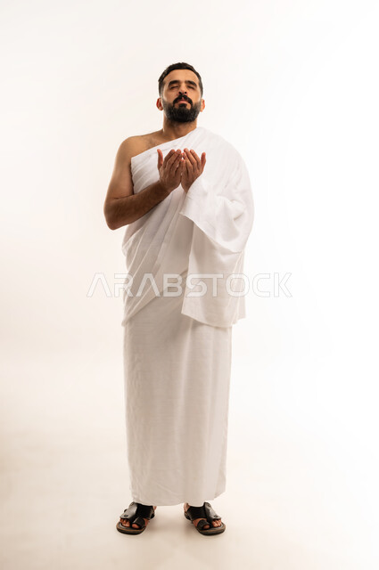 مفهوم التضرع والعبادة , التقرب الى الله بالأعمال الصالحة, أدعية وأذكار اسلامية ، الركن الخامس من أركان الاسلام ،  بورتريه لرجل عربي عماني خليجي يرتدي ملابس الإحرام ، يرفع يديه للأعلى ويدعى بخشوع ، الاجتهاد بالأدعية والطاعات ، الجسم بالطول الكامل، خلفية بيضاء .