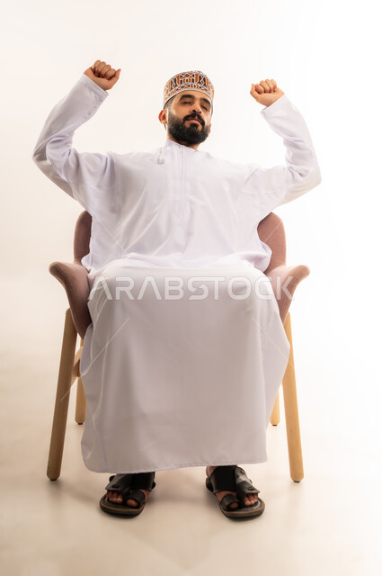 الشعور بالتعب والحاجة الى النوم والراحة, ايماءات النعاس والارهاق ، الإحساس بالكسل والخمول ، بورتريه  لشاب عربي خليجي عماني يرتدي الدشداشة والكمه ، خلفية بيضاء .